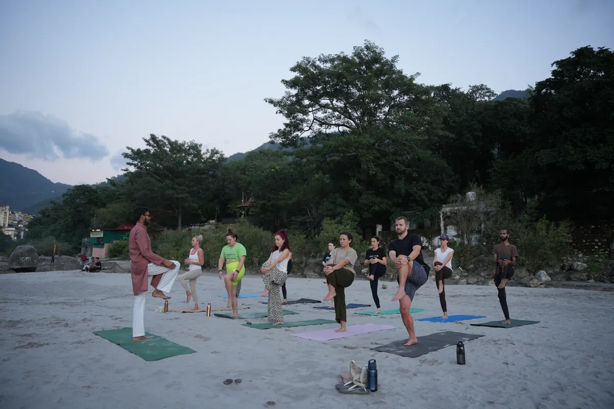 Yoga teacher training group gathered for an outdoor class on the riverbank in Rishikesh