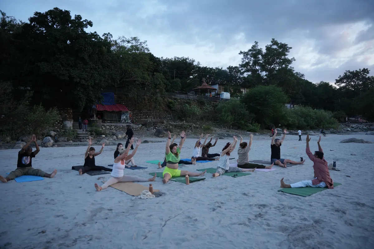 Ashtanga yoga class practising with arms raised at sunrise beside the Ganges in Rishikesh
