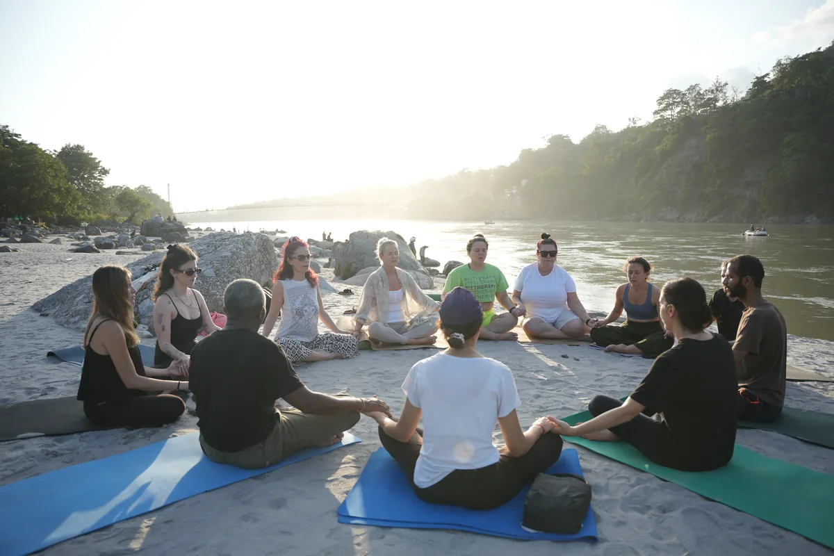 Meditation students sitting together at sunrise on the banks of the Ganges in Rishikesh