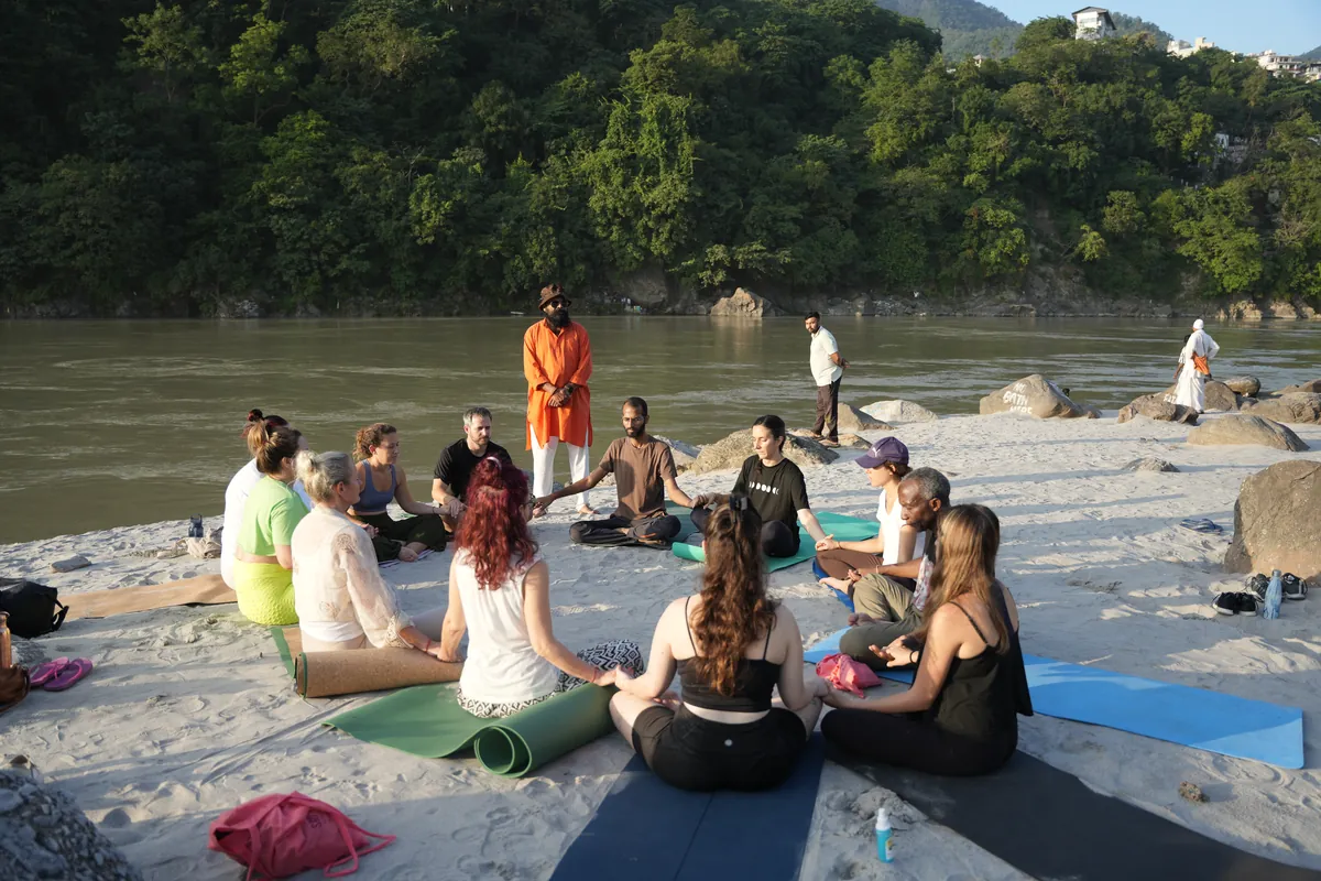 Yoga retreat group sitting together on the sand beside the Ganges river in Rishikesh