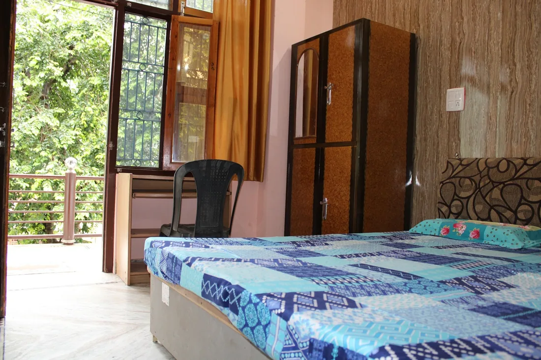 Bright guest room with double bed, wardrobe and balcony door at Rishikesh yoga ashram