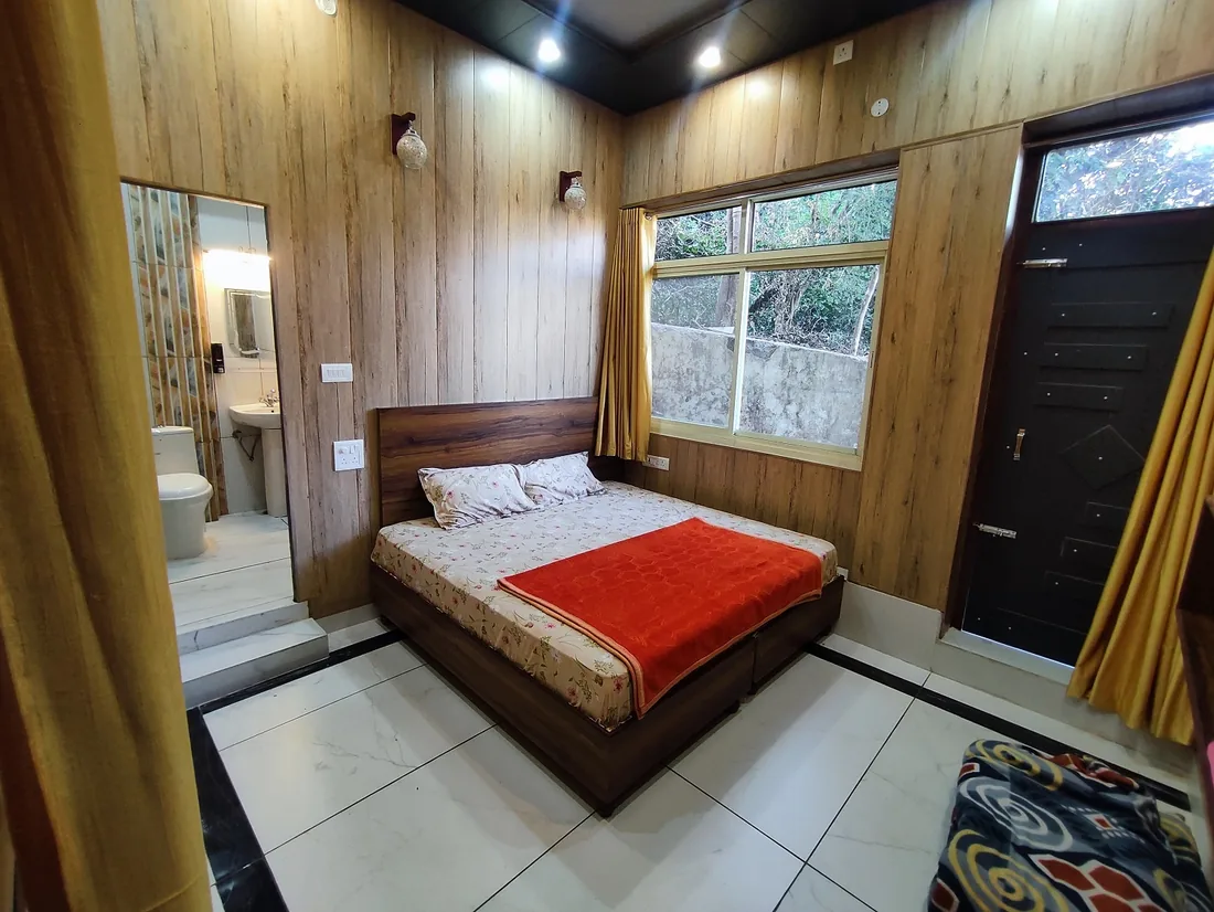 Guest room at Sri Yoga Ashram Rishikesh with double bed, ensuite bathroom and window onto trees