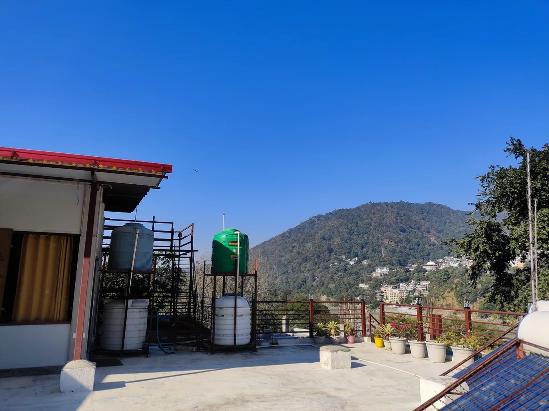Rooftop terrace at Sri Yoga Ashram with potted plants and forested Rishikesh hill views