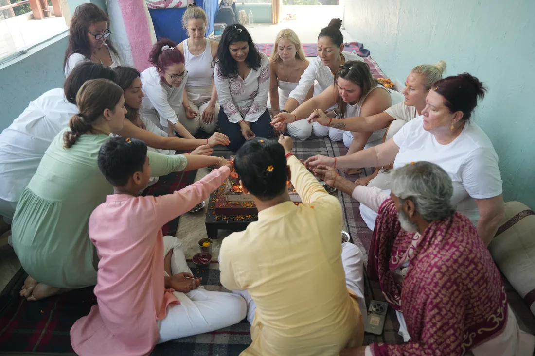 Students and a priest gathered around a small fire puja altar at Sri Yoga Ashram Rishikesh