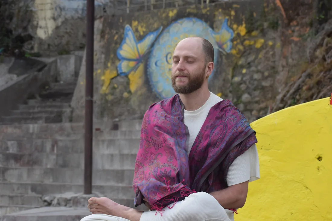 Bearded man in shawl meditating with eyes closed near painted wall in Rishikesh