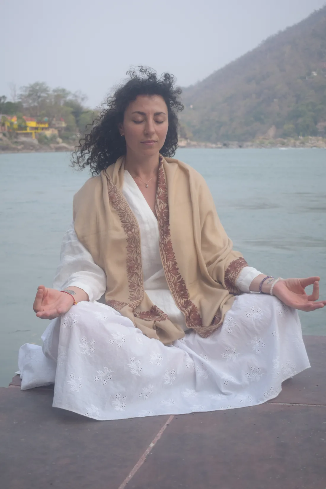 Woman meditating in lotus pose beside the Ganges river at Rishikesh in white clothing