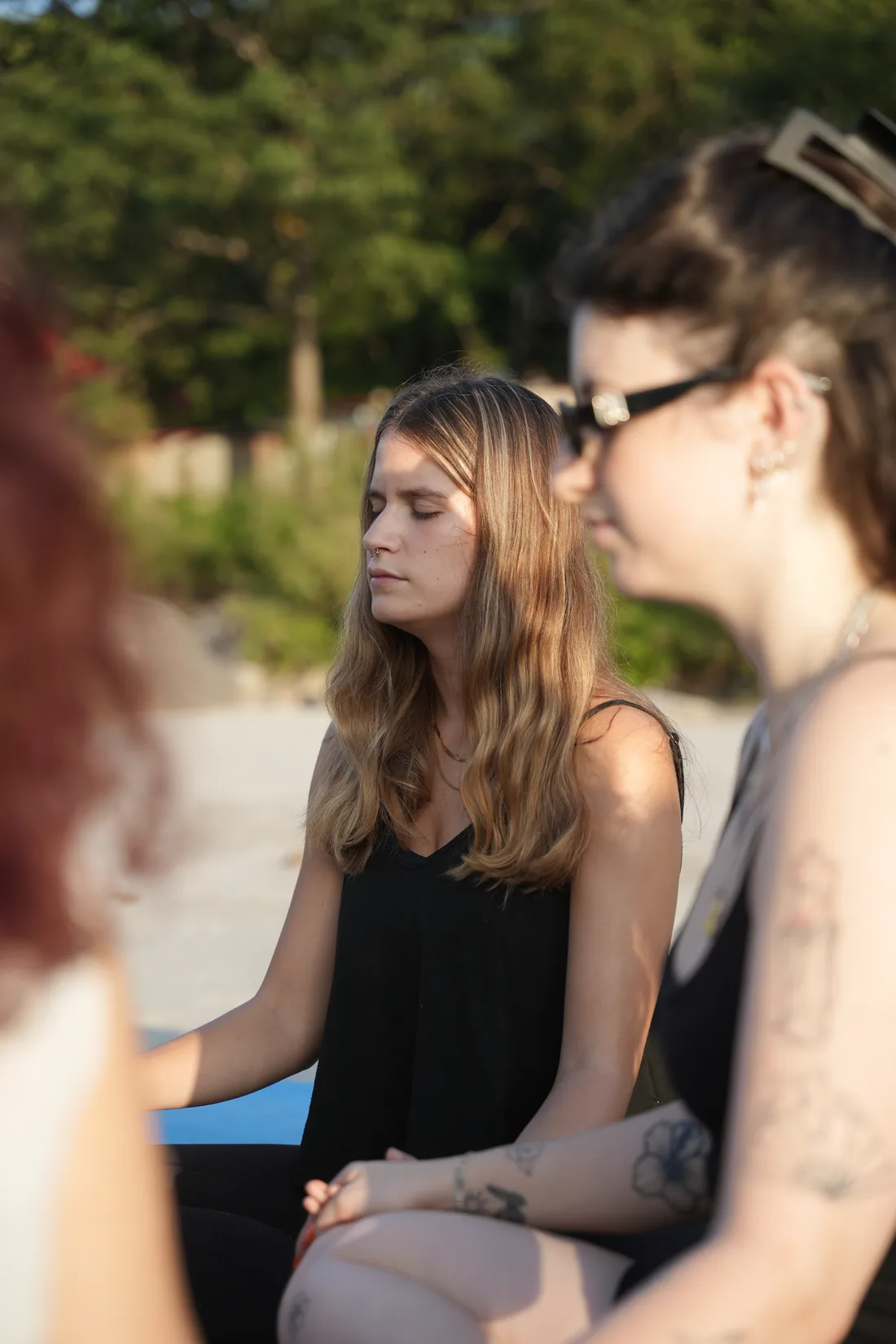 Students meditating with eyes closed on a sandy riverbank in warm evening light, Rishikesh