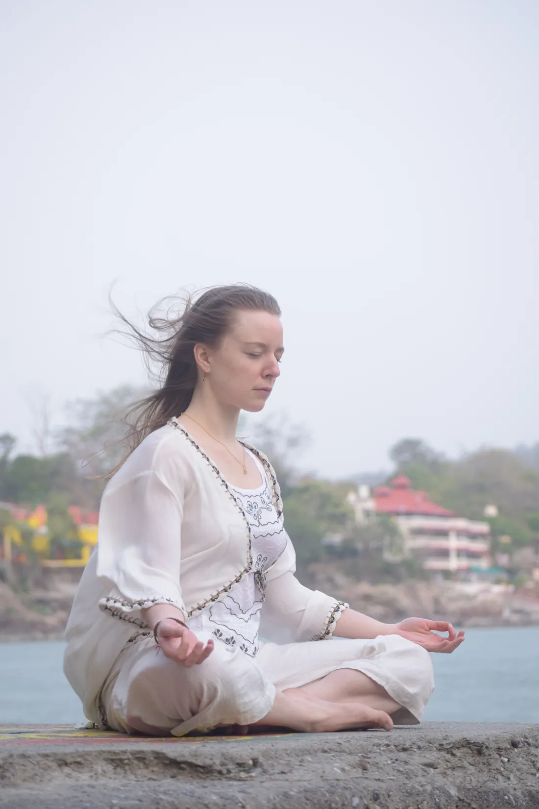 Student sits in lotus meditation on a rock above the Ganges in Rishikesh