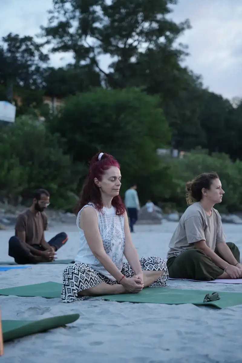 Student meditating cross legged at dusk on the sandy Ganga riverbank in Rishikesh