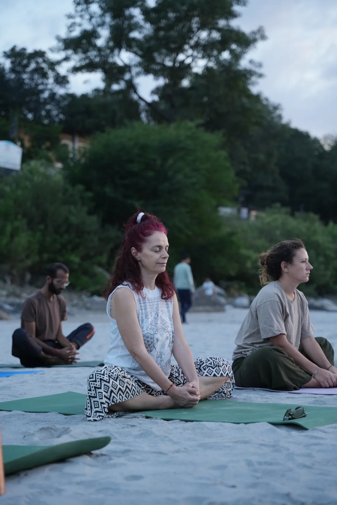 Student meditating cross legged at dusk on the sandy Ganga riverbank in Rishikesh