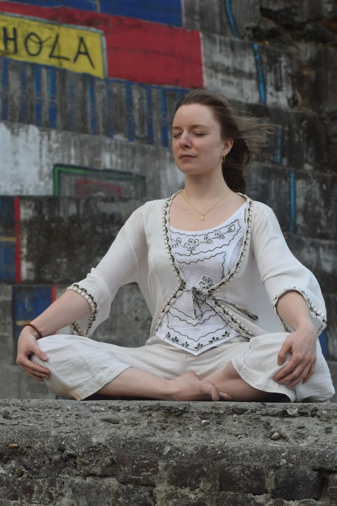 Woman meditating cross legged on a stone ledge by painted steps in Rishikesh