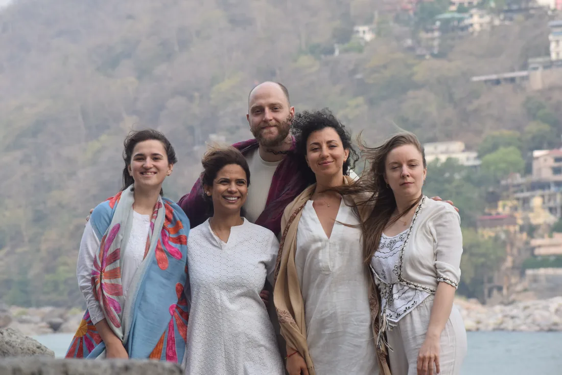 Five smiling yoga teacher training students together above the Ganges river in Rishikesh