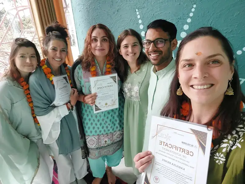 Graduates hold 200 hour yoga teacher training certificates with marigold garlands at Sri Yoga Ashram