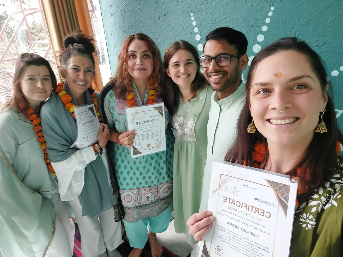 Graduates hold 200 hour yoga teacher training certificates with marigold garlands at Sri Yoga Ashram