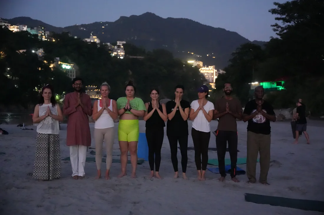 Group of yoga students standing in namaste at dusk on Rishikesh riverbank