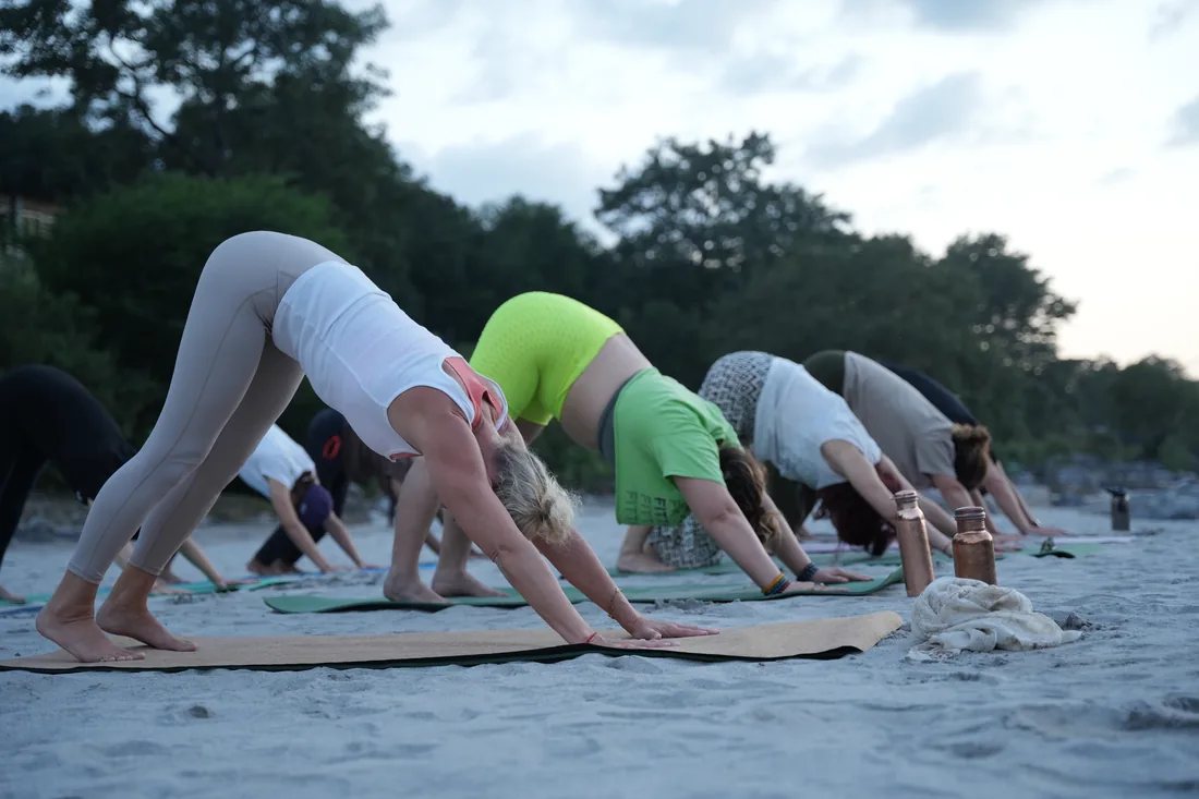 Yoga students in downward dog on Ganga riverbank sand at dusk, Rishikesh