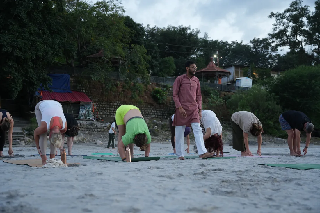 Sri Yoga Ashram teacher guiding students through standing forward fold beside the Ganga